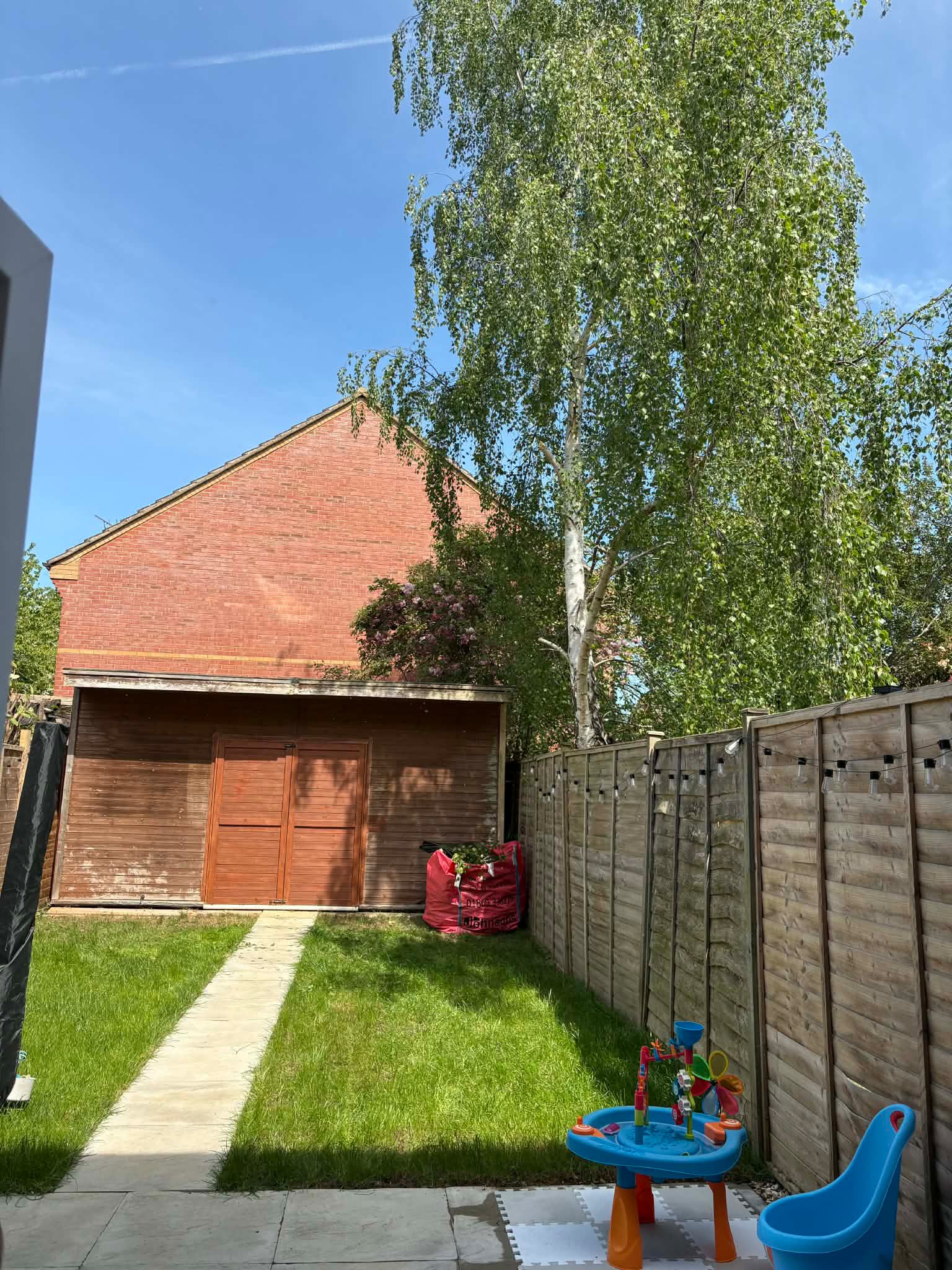 A tidy rear lawn with a clean paved path leading to a shed